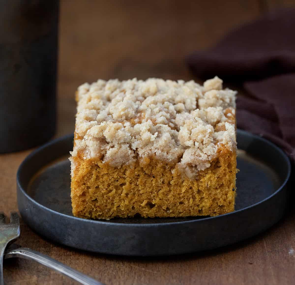 One piece of Pumpkin Streusel Sheet Cake on a small black plate on a wooden table.