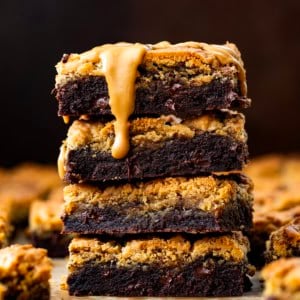 Stack of Peanut Butter Brookies on a wooden table surrounded by more and with a peanut butter drizzle.