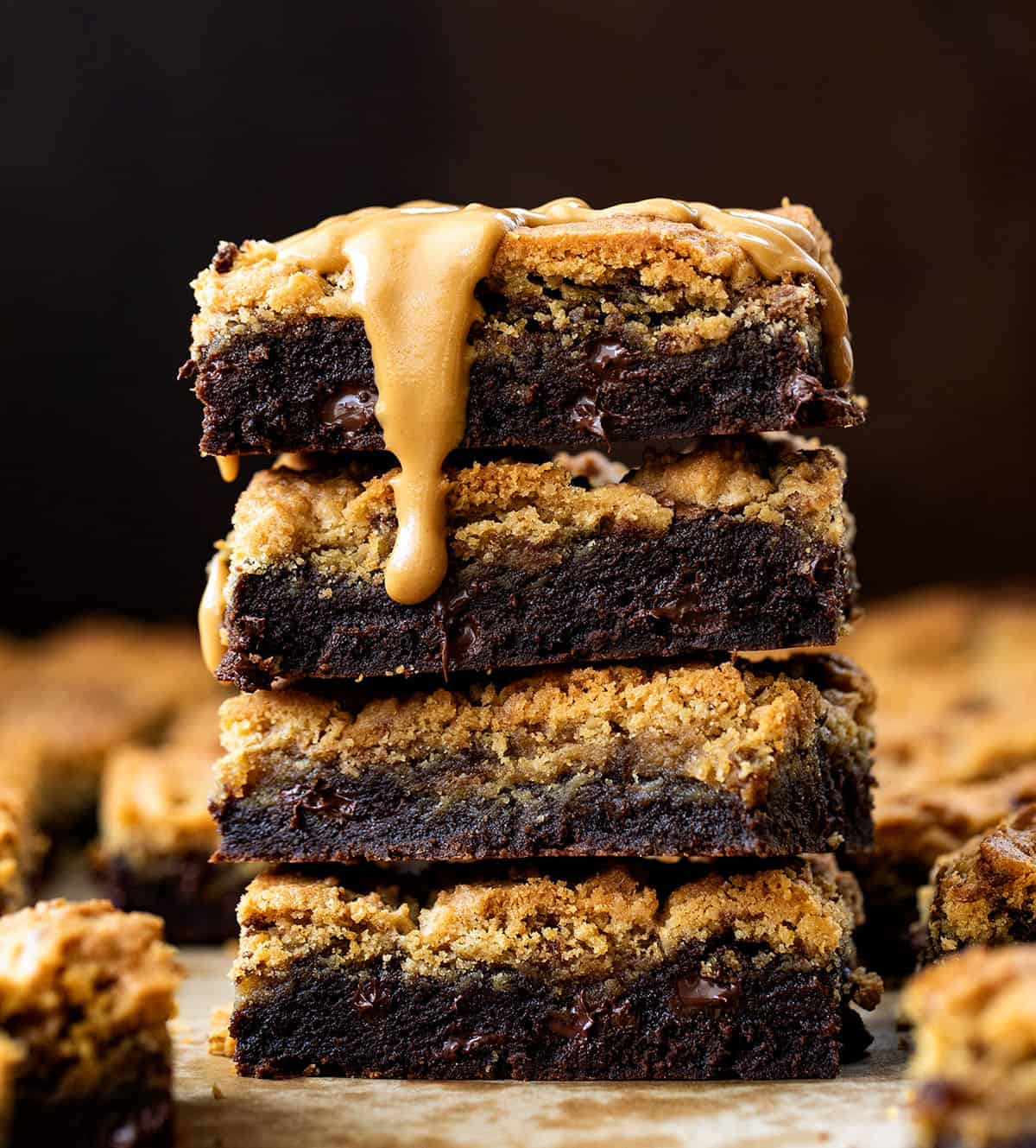Stack of Peanut Butter Brookies on a wooden table surrounded by more and with a peanut butter drizzle.