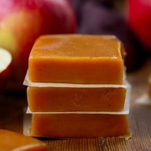 Stack of Apple Cider Caramels on a wooden table with apples around it.