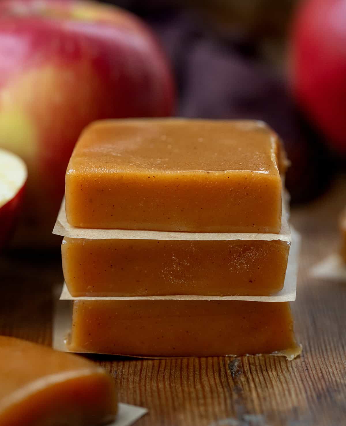 Stack of Apple Cider Caramels on a wooden table with apples around it.