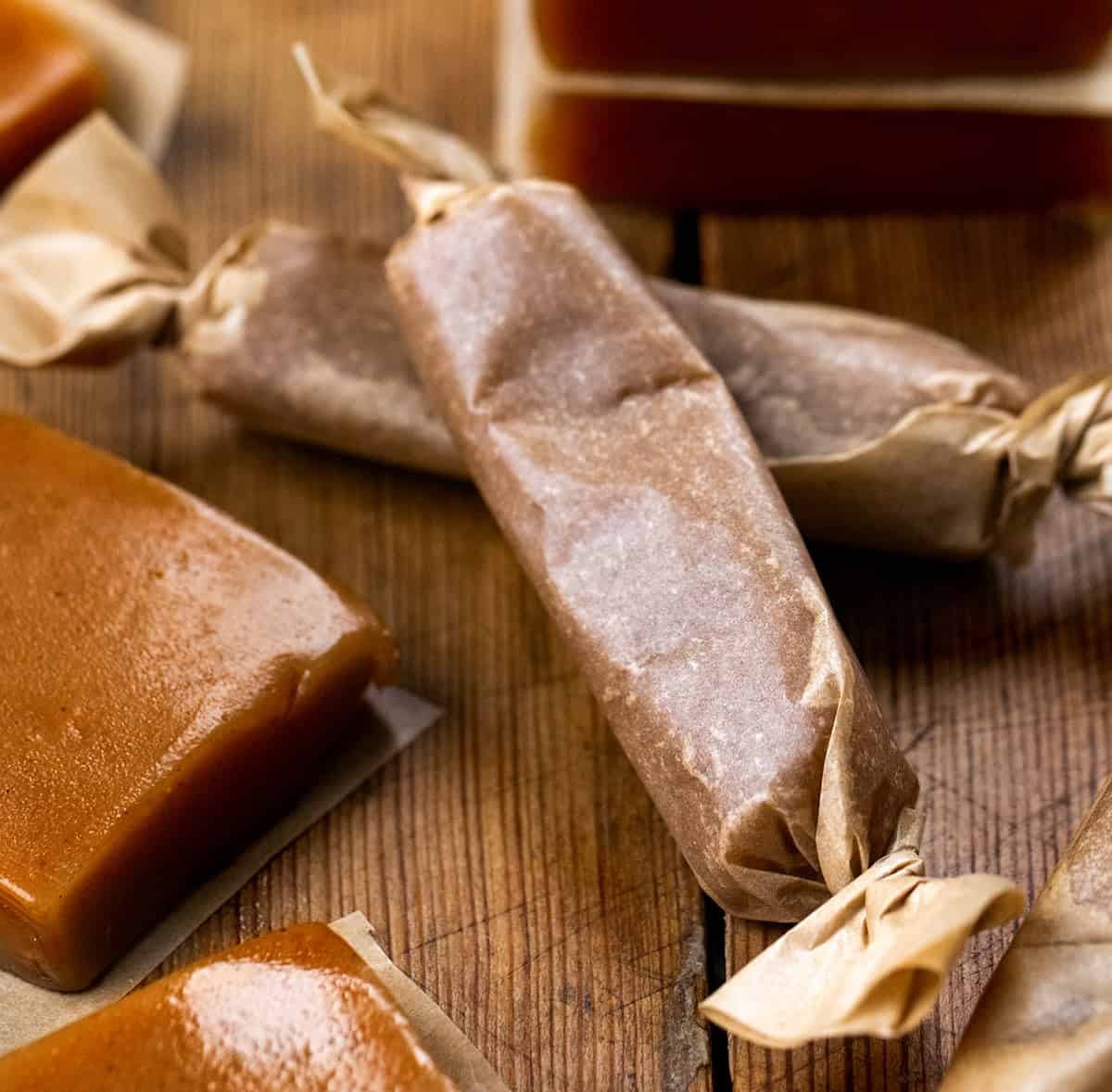 Apple Cider Caramels rolled in parchment with more caramels around it.