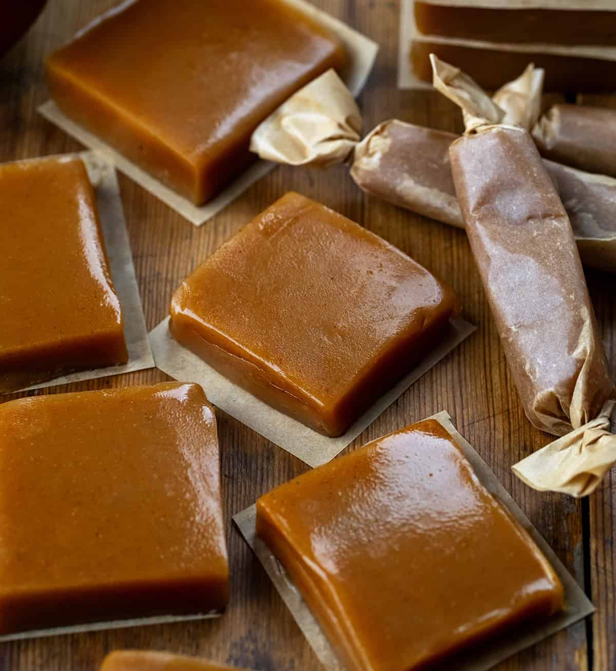 Apple Cider Caramel squares on parchment with some packaged in parchment nearby.
