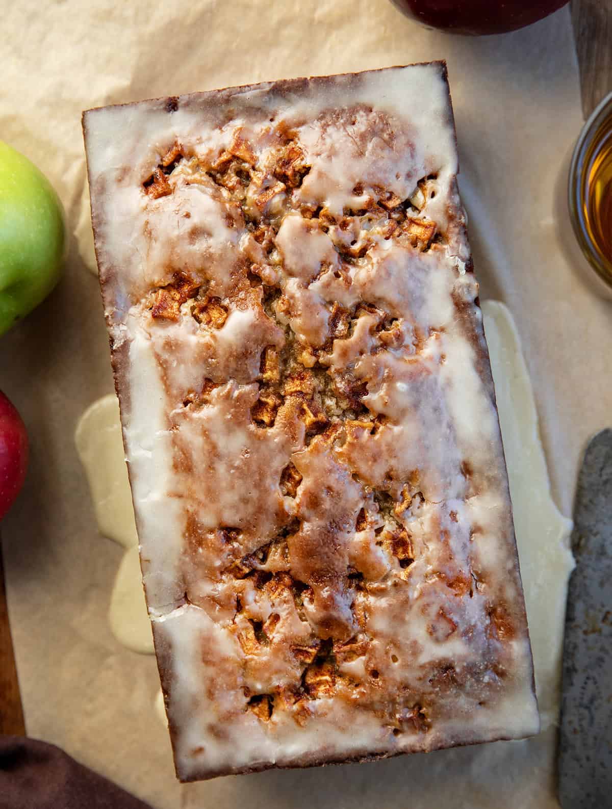 Loaf of Apple Cider Fritter Bread on a wooden table from overhead with a glass of apple cider and apples.