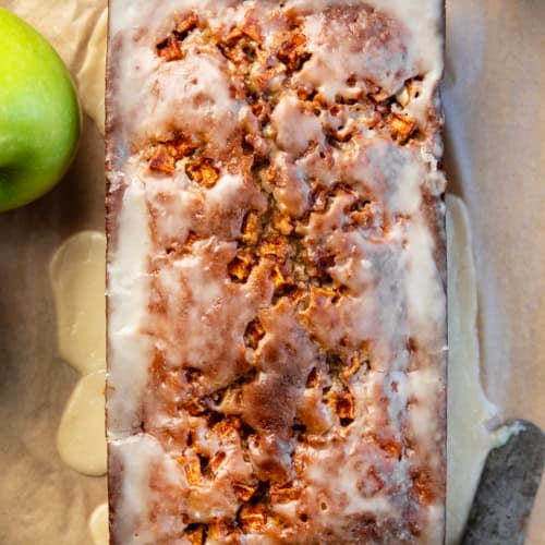 Loaf of Apple Cider Fritter Bread on a wooden table from overhead with a glass of apple cider and apples.