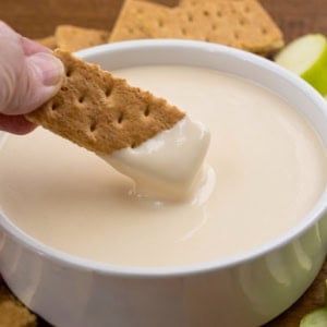 Dipping a graham cracker into Apple Cider Marshmallow Sauce in a white bowl.