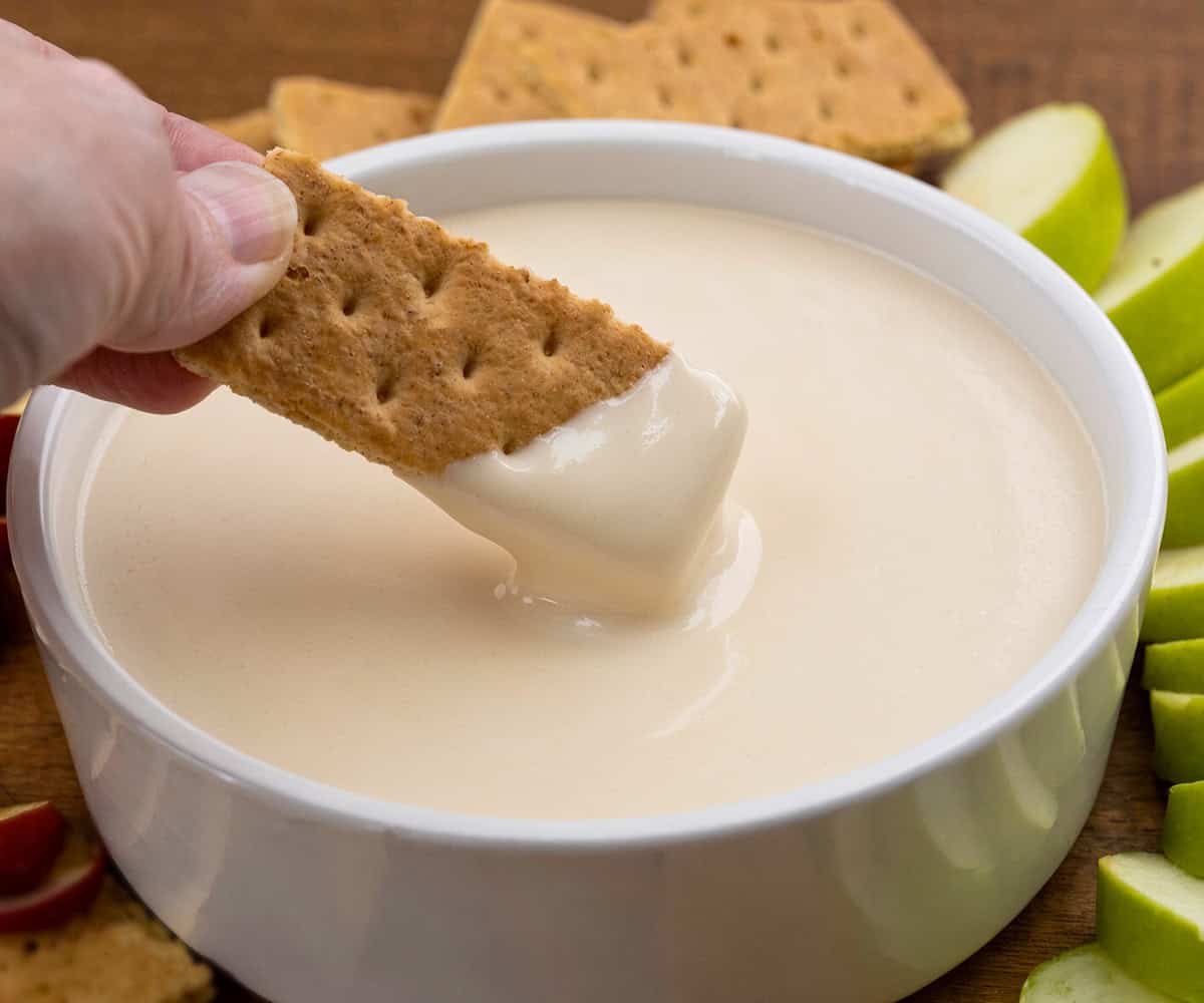 Dipping a graham cracker into Apple Cider Marshmallow Sauce in a white bowl.