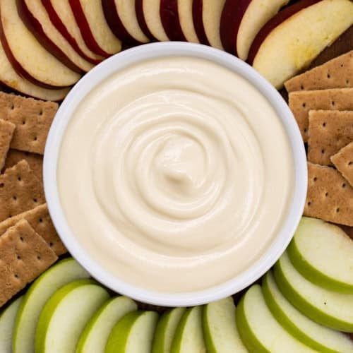 Bowl filled with Apple Cider Marshmallow Sauce surrounded by graham crackers and sliced apples.
