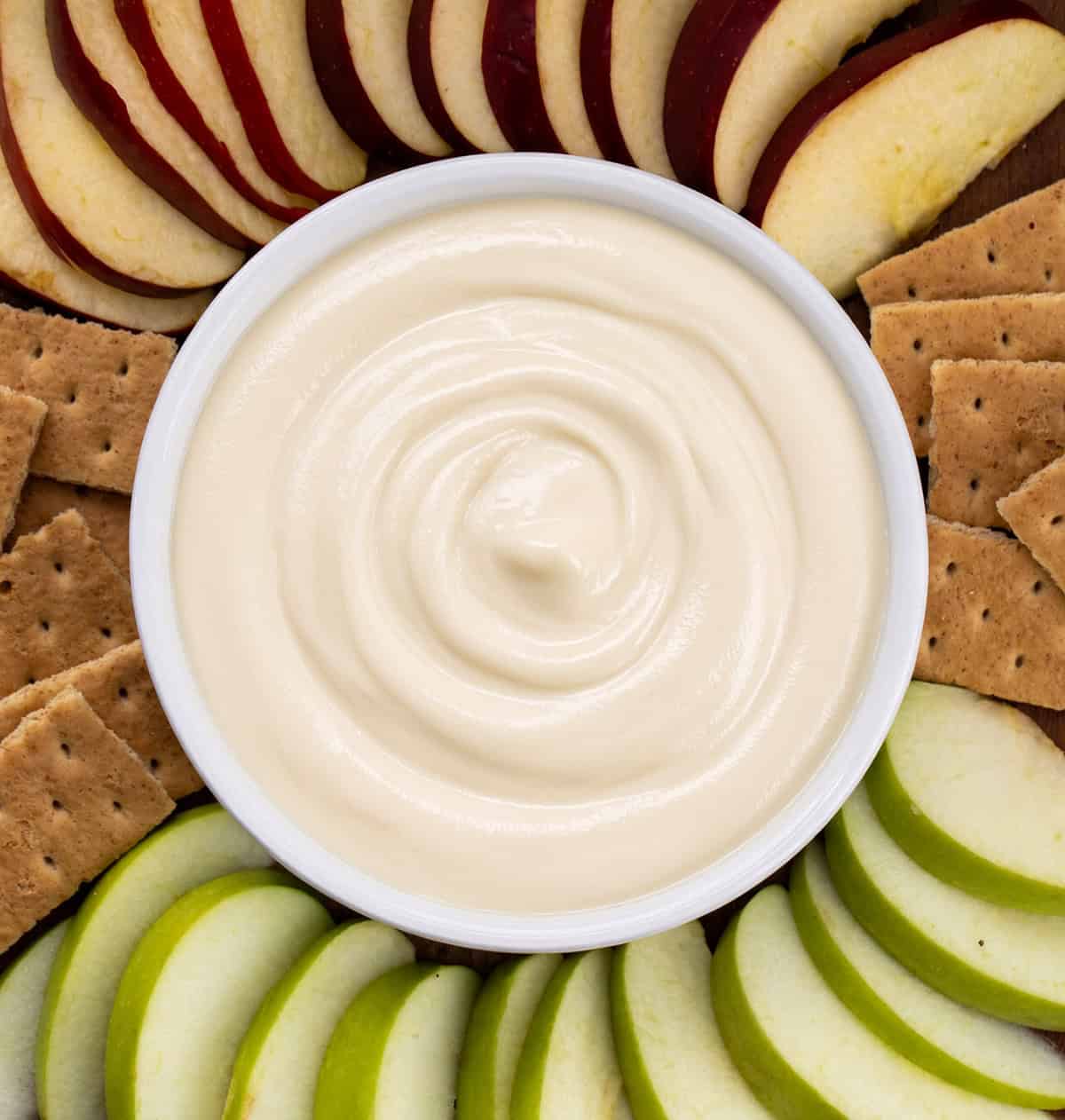 Bowl filled with Apple Cider Marshmallow Sauce surrounded by graham crackers and sliced apples.