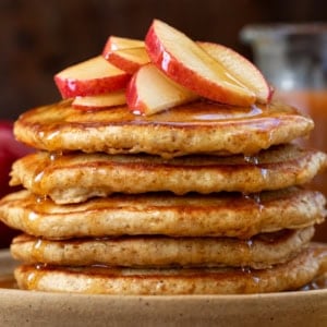 Stack of Apple Cider Pancakes with apple cider syrup in the background.