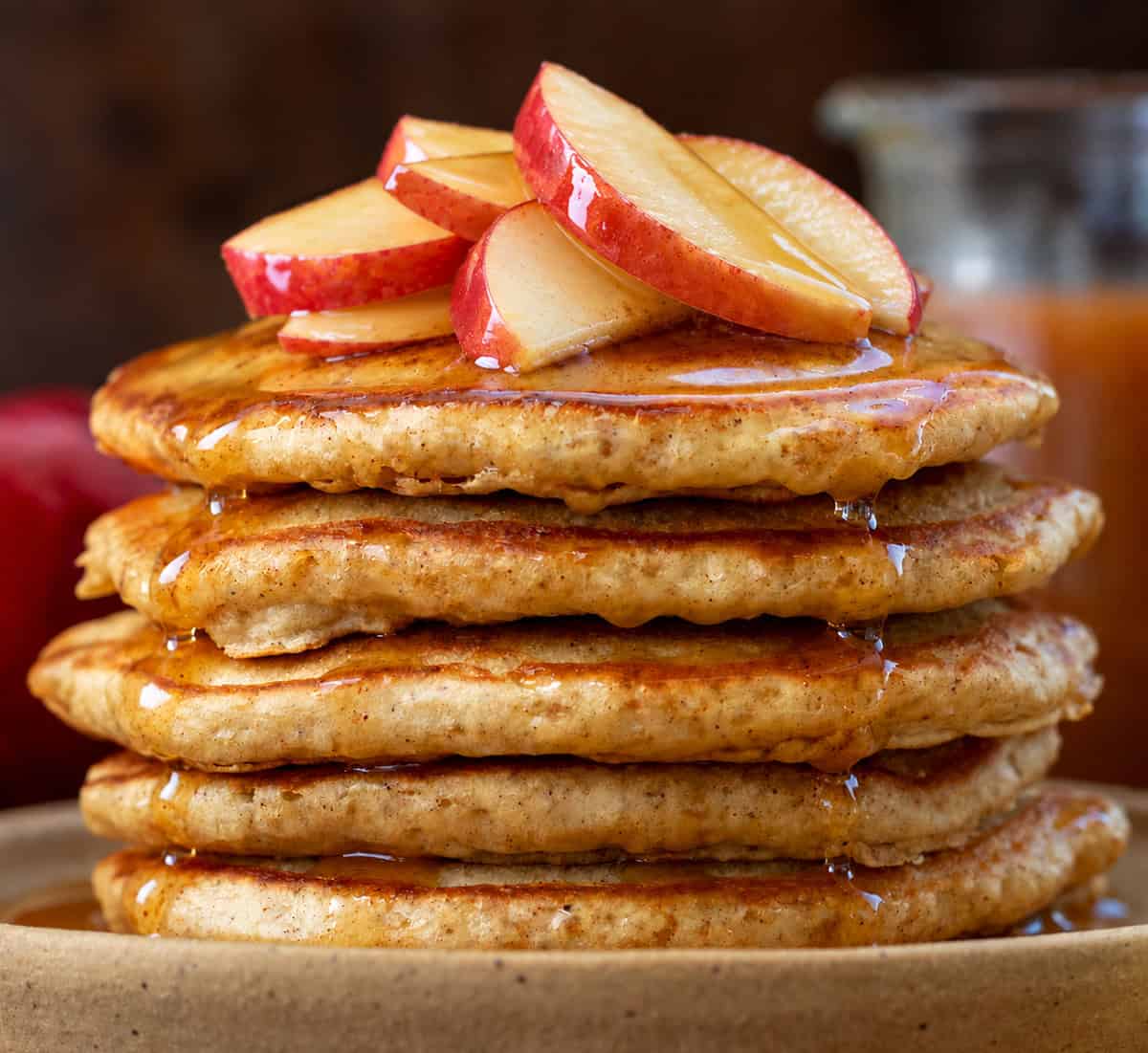 Stack of Apple Cider Pancakes with apple cider syrup in the background.