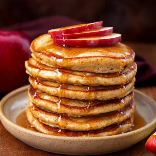 Stack of Apple Cider Pancakes with apple slices and syrup over top.