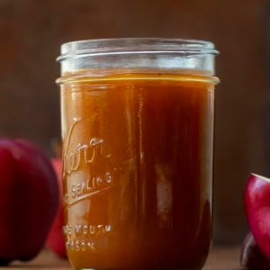 Jar of Apple Cider Syrup on a wooden table with apples.