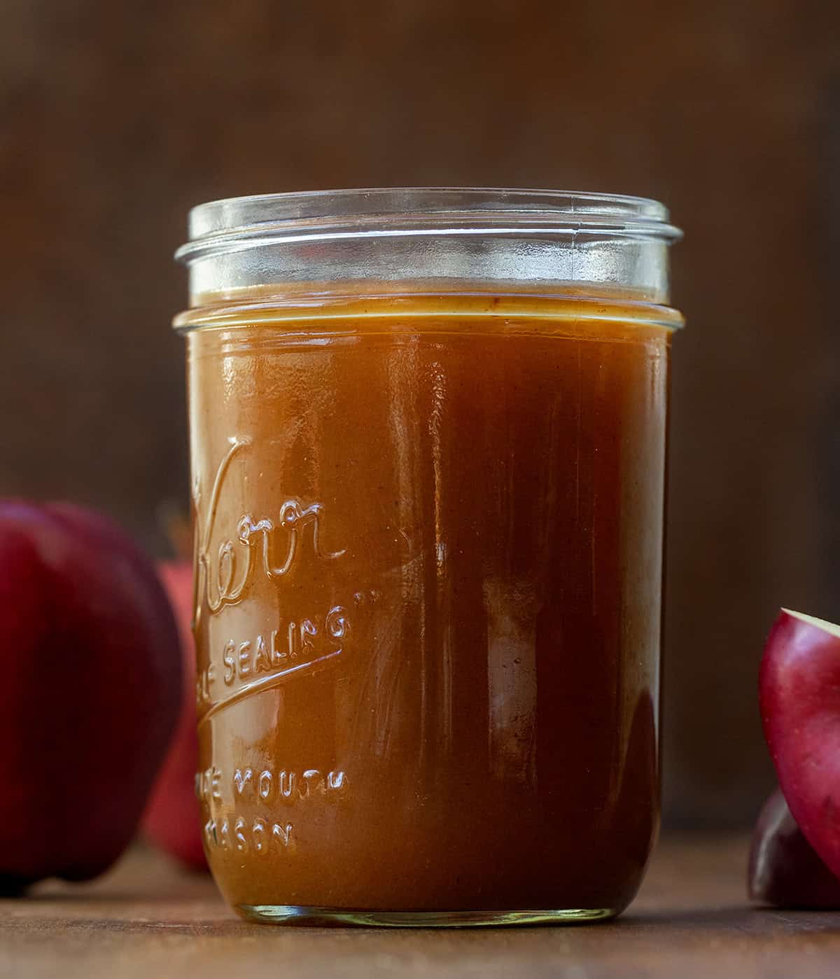 Jar of Apple Cider Syrup on a wooden table with apples.