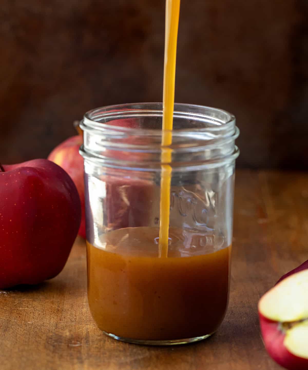 Pouring Apple Cider Syrup into a glass mason jar.