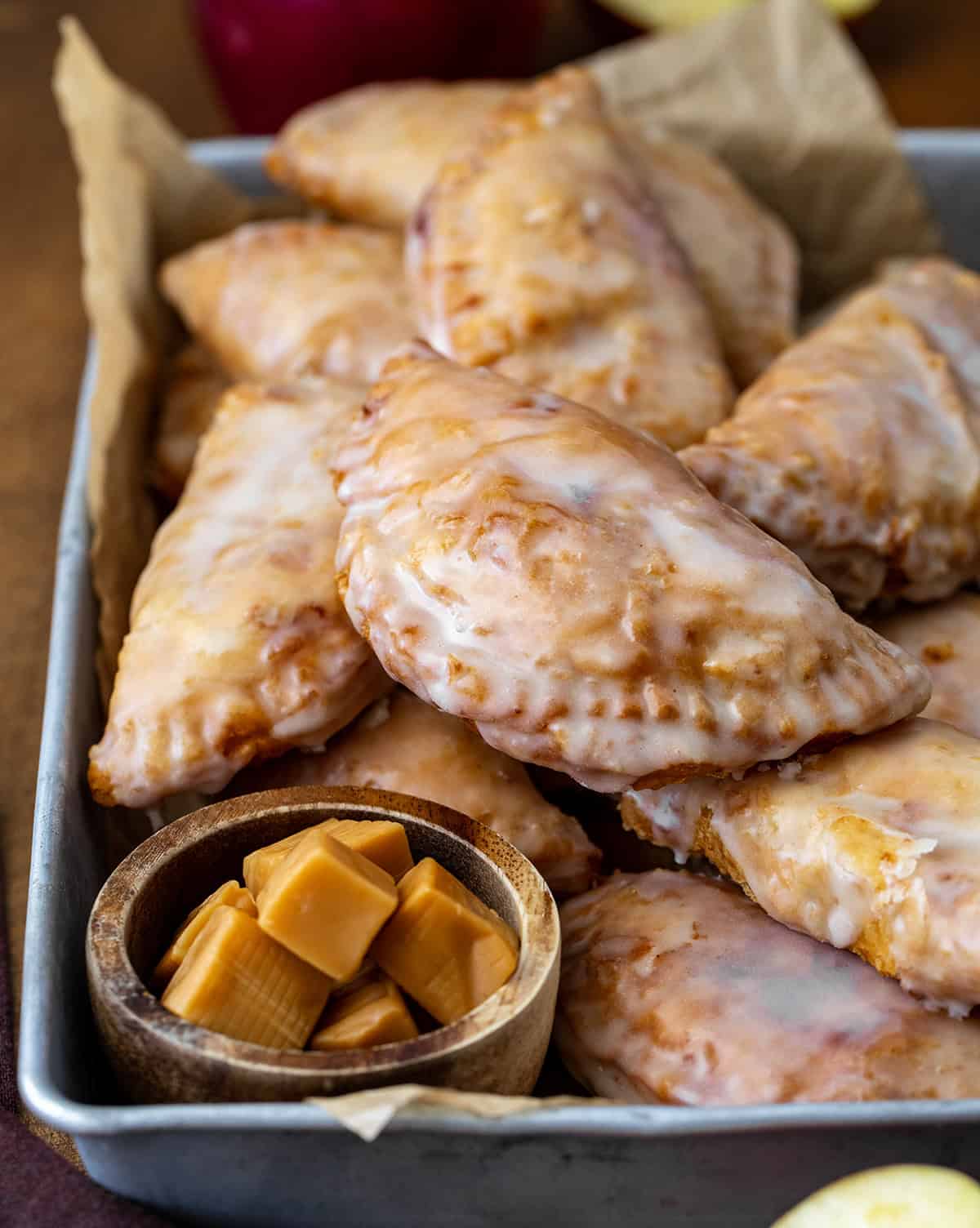 Caramel Apple Hand Pies in a platter with caramels and apples on a wooden table.