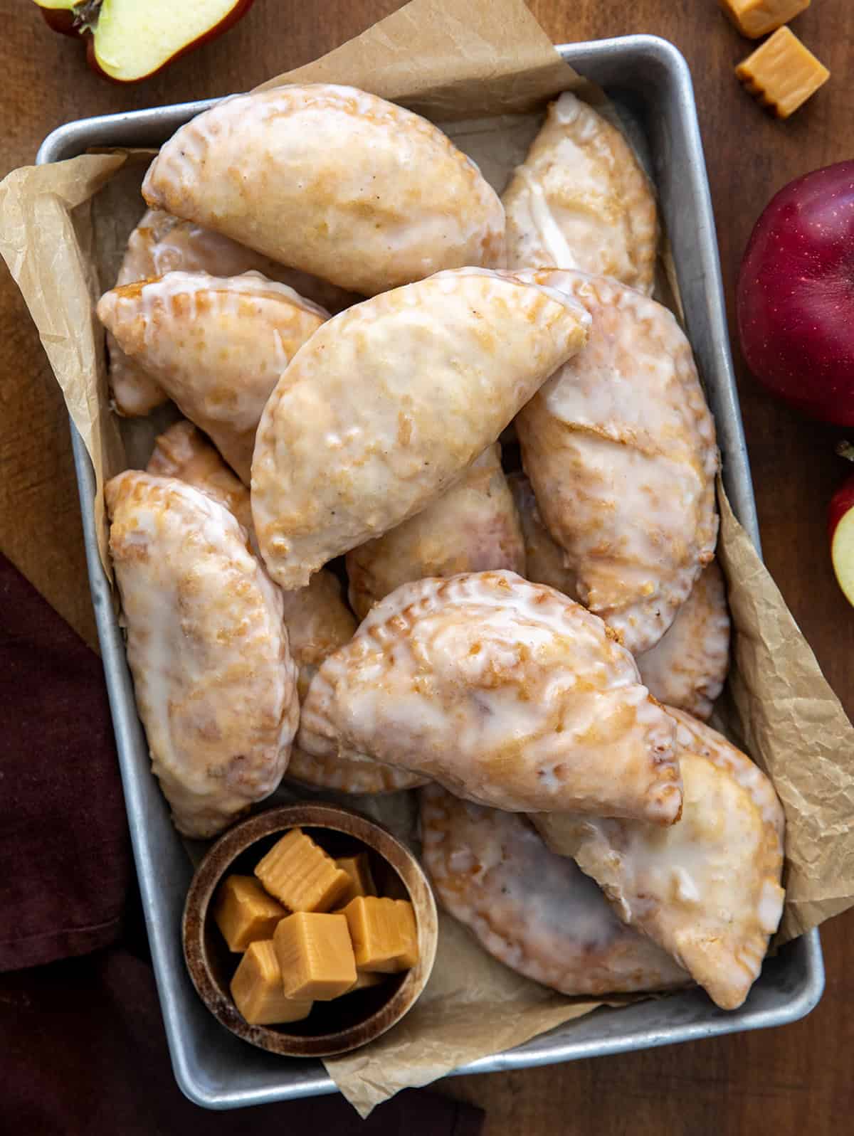 Caramel Apple Hand Pies on a wooden table from overhead with caramels and apples.