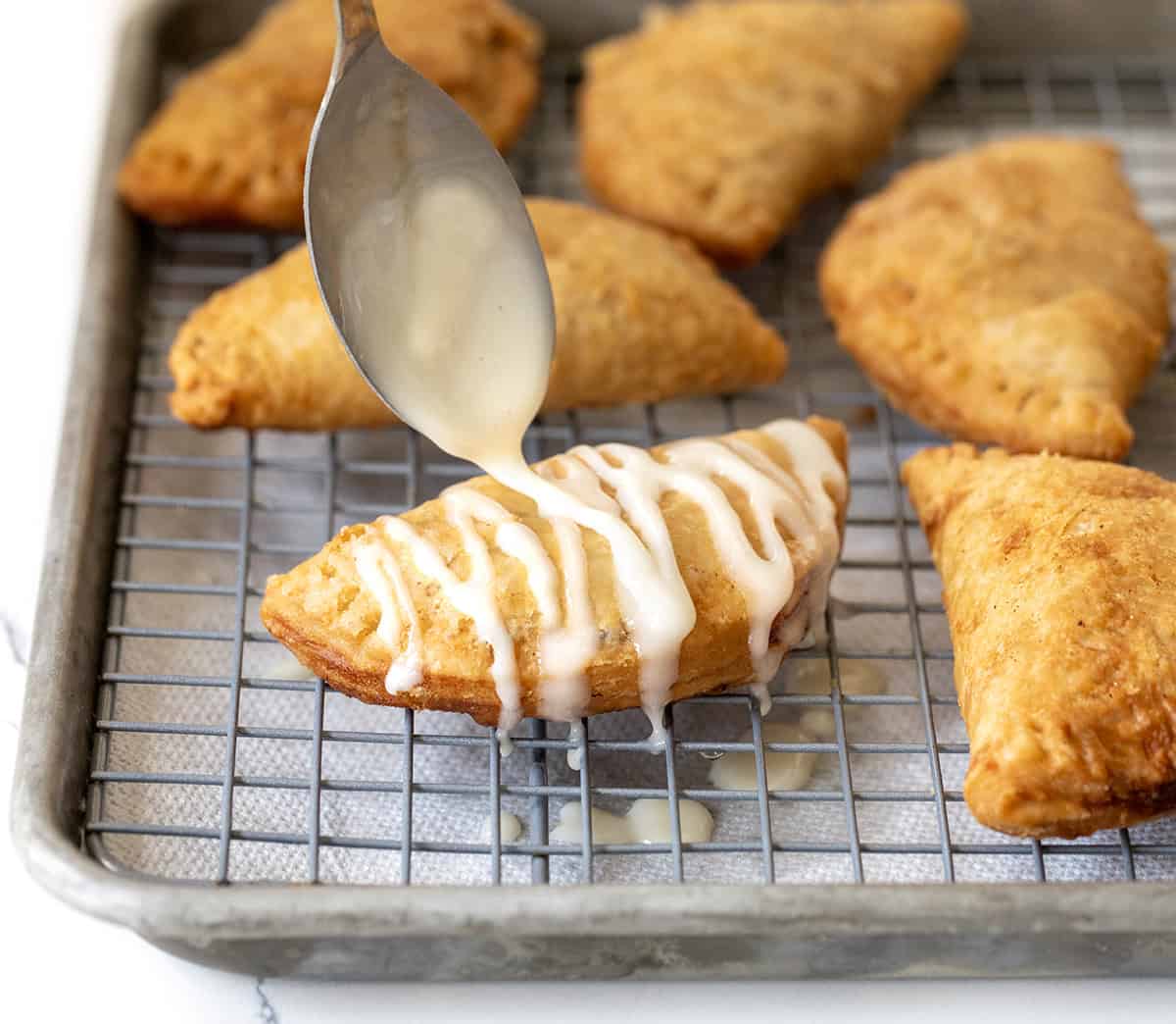 Drizzling glaze over a Caramel Apple Hand Pie.