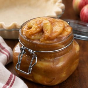 Jar of Caramel Apple Pie Filling in front of a pie crust and apples.