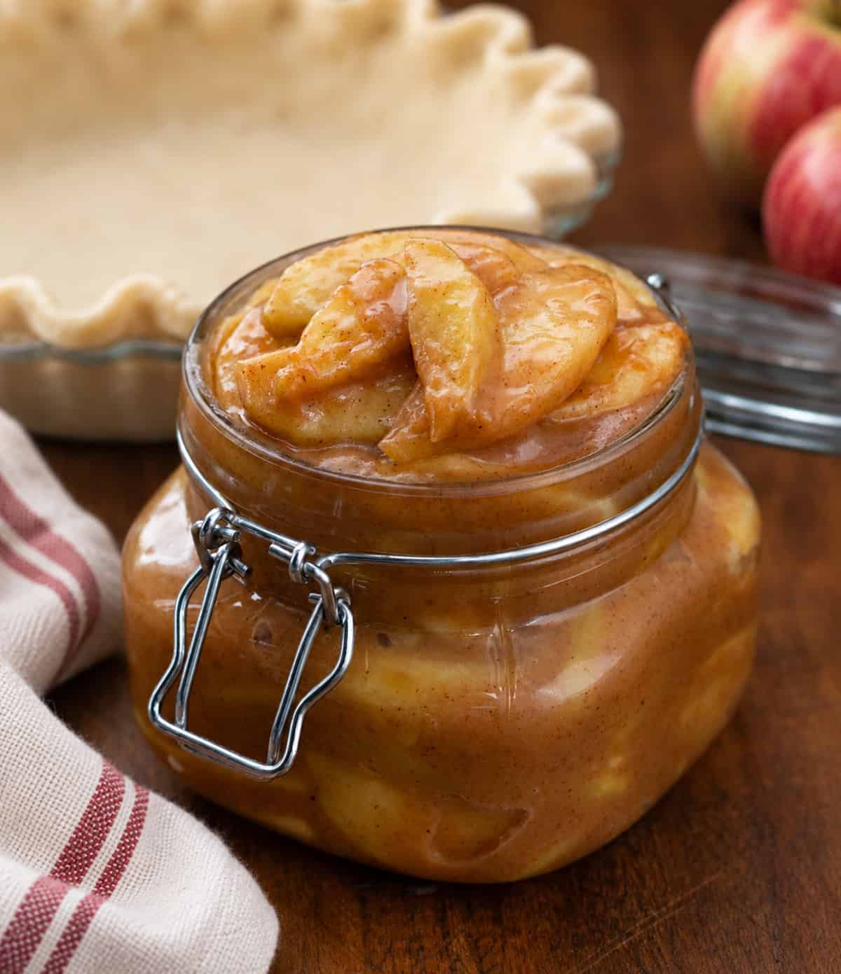 Jar of Caramel Apple Pie Filling in front of a pie crust and apples.