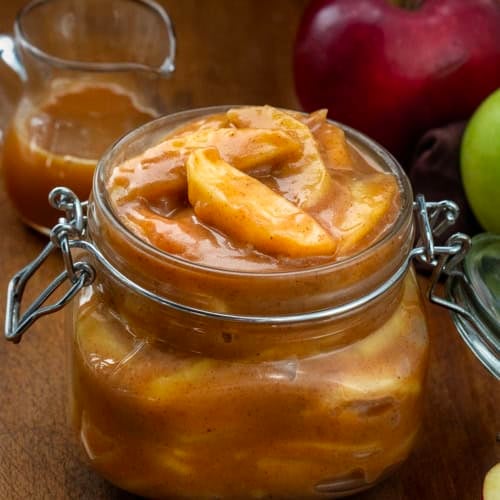 Caramel Apple Pie Filling in a jar with caramel and apples behind it.