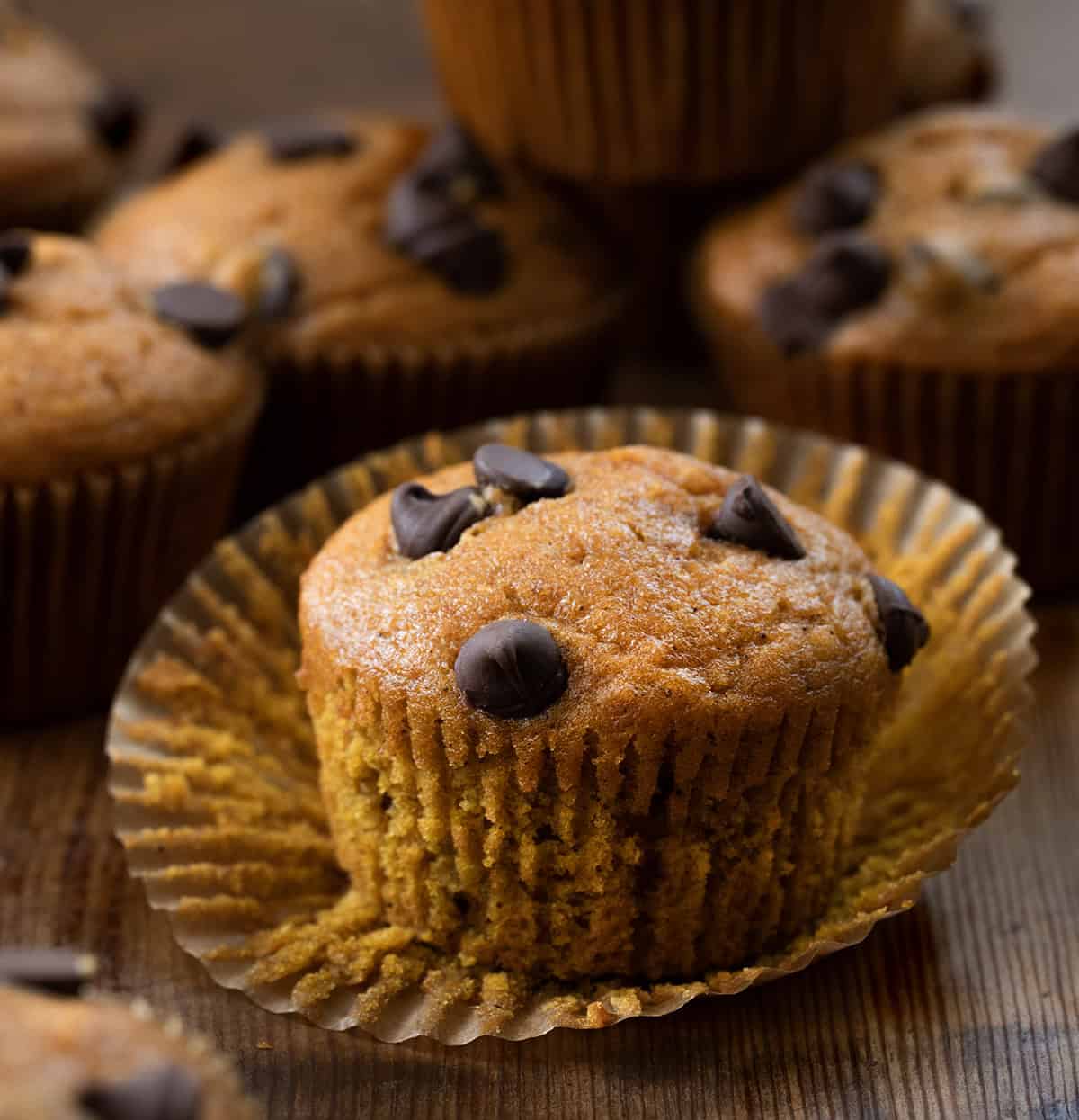 Chocolate Chip Pumpkin Muffin with the wrapped peeled away on a wooden table.