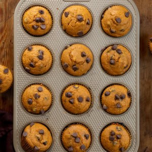 Chocolate Chip Pumpkin Muffins in the muffin pan on a wooden table from overhead.