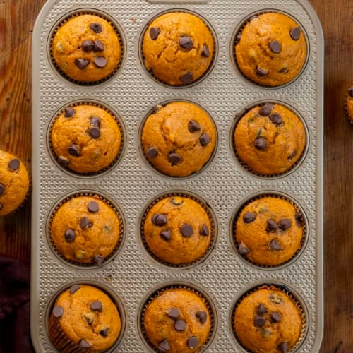 Chocolate Chip Pumpkin Muffins in the muffin pan on a wooden table from overhead.