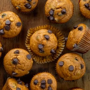 Chocolate Chip Pumpkin Muffins on a wooden table with the center muffin unwrapped and sitting on the wrapper.