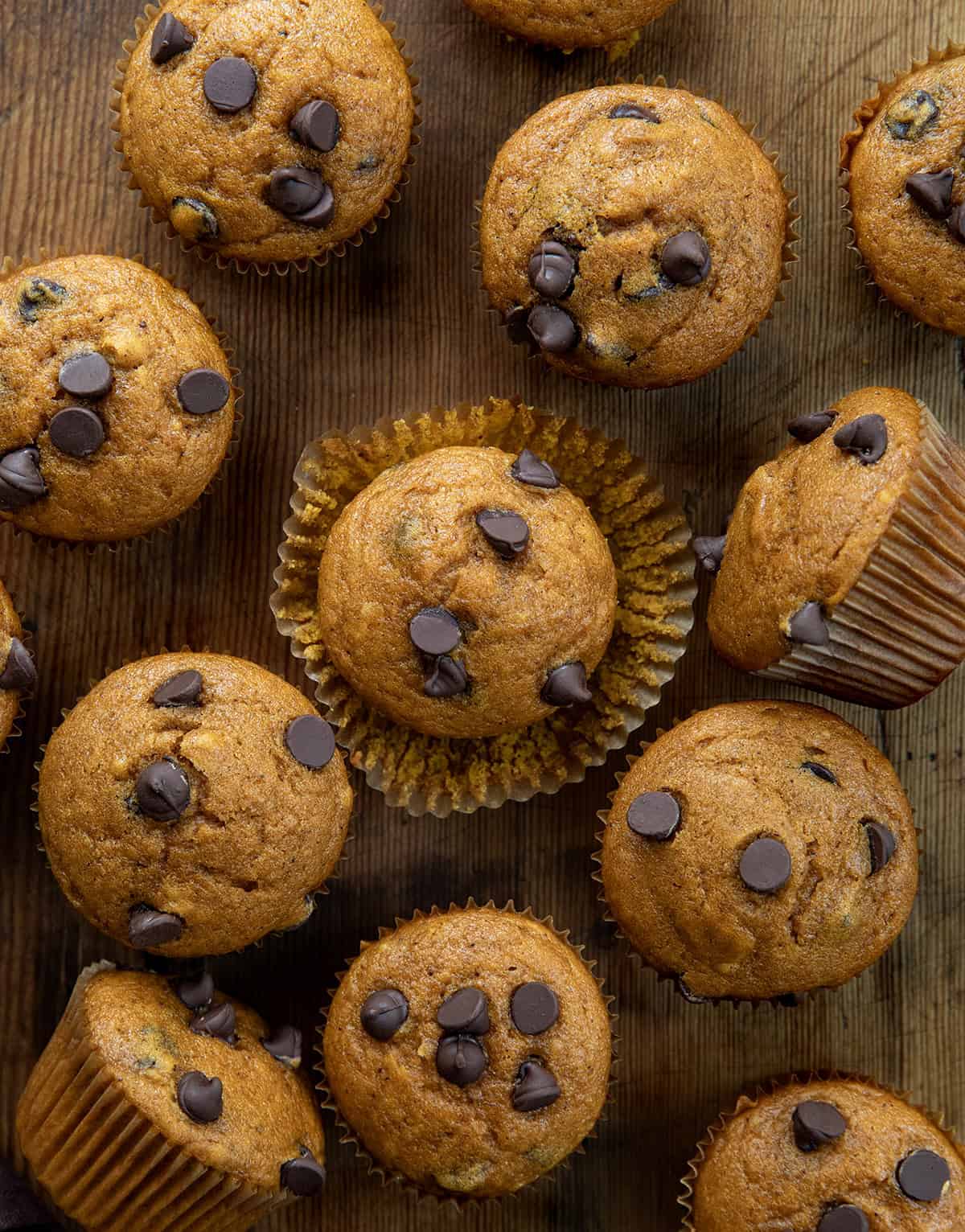 Chocolate Chip Pumpkin Muffins on a wooden table with the center muffin unwrapped and sitting on the wrapper.