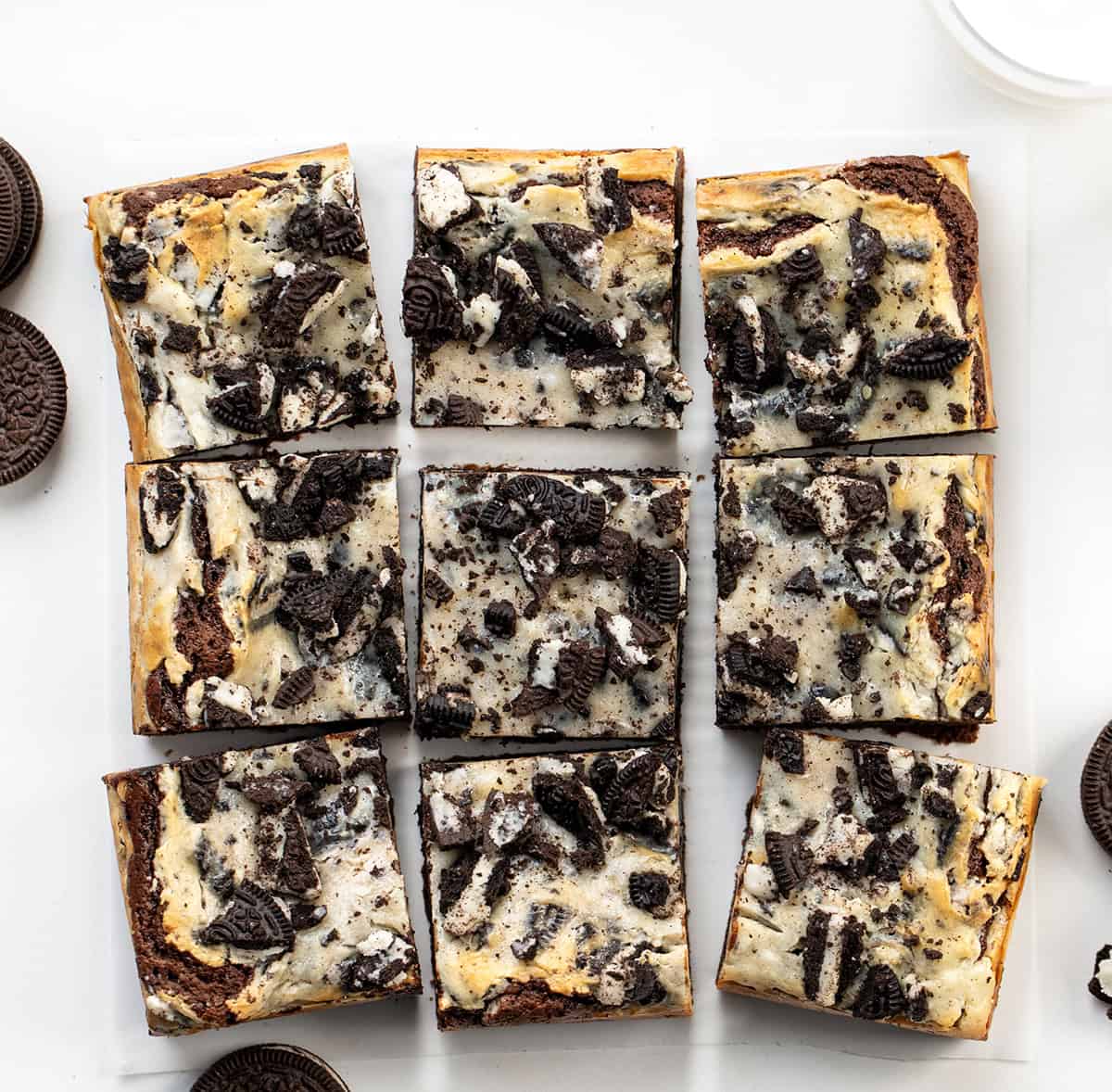 Cookies and Cream Brownies cut into squares on a white table surrounded by Oreos from overhead.