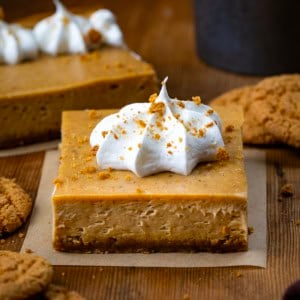 Gingerbread Cheesecake Bar squares on a wooden table with gingersnap cookies.