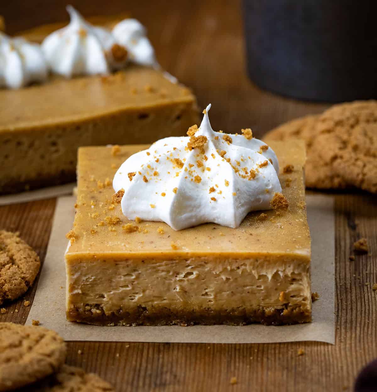 Gingerbread Cheesecake Bar squares on a wooden table with gingersnap cookies.