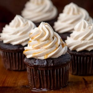 Chocolate cupcakes with piped Maple Ermine Frosting on them and one with syrup drizzled over top.