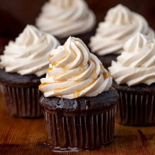 Chocolate cupcakes with piped Maple Ermine Frosting on them and one with syrup drizzled over top.