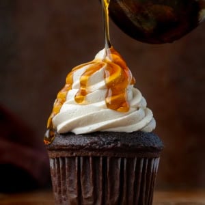 Drizzling syrup over a cupcake with Maple Ermine Frosting piped on it.