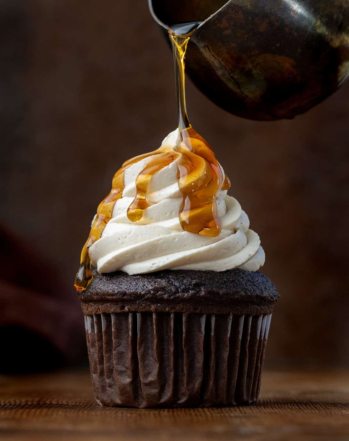 Drizzling syrup over a cupcake with Maple Ermine Frosting piped on it.