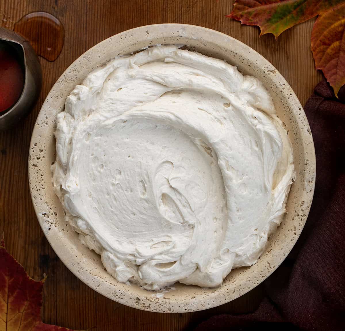 Bowl of Maple Ermine Frosting on a wooden table with maple leaves and maple syrup Bowl of Maple Ermine Frosting on a wooden table with maple leaves and maple syrup.
