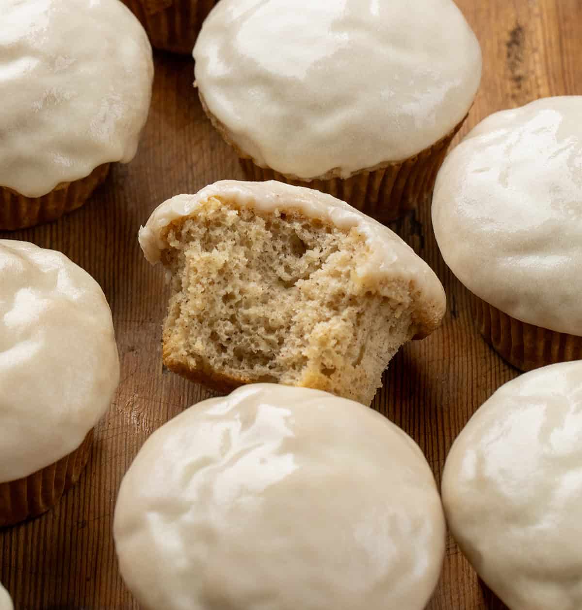 Maple Glazed Donut Muffins on a wooden table with the center muffin bit into showing the inside texture.