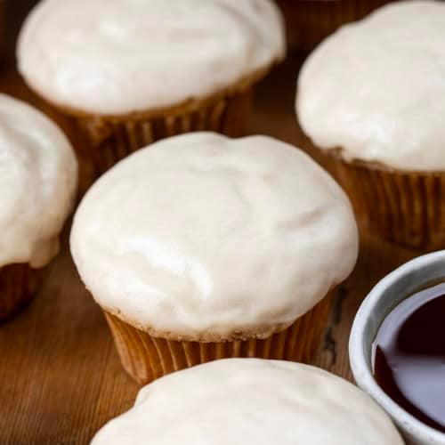 Close up of Maple Glazed Donut Muffins next to maple syrup.