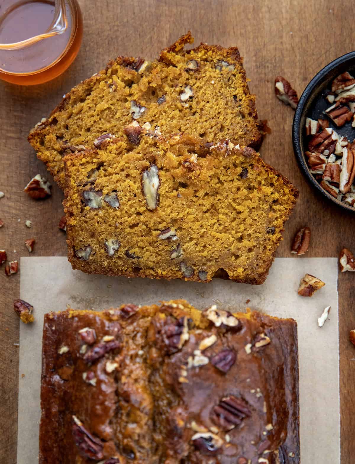 Loaf of Maple Pecan Pumpkin Bread on a wooden table with a couple of slices cut and laying flat Loaf of Maple Pecan Pumpkin Bread on a wooden table with a couple of slices cut and laying flat.