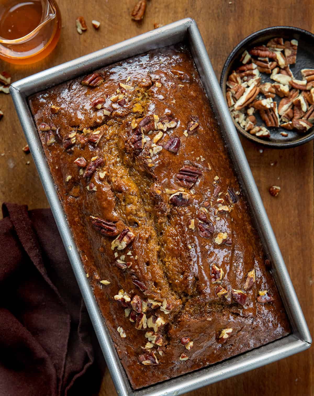 Loaf of Maple Pecan Pumpkin Bread on a wooden table surrounded by syrup and pecans from overhead Loaf of Maple Pecan Pumpkin Bread on a wooden table surrounded by syrup and pecans from overhead.