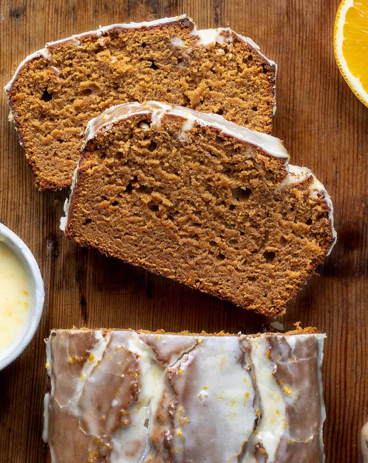 Pieces of Orange Gingerbread Loaf laying flat on a wooden table next to the cut loaf.