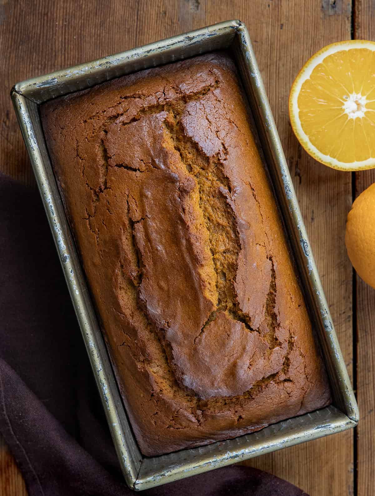 Gingerbread Loaf in the pan on a wooden table from overhead with fresh oranges.
