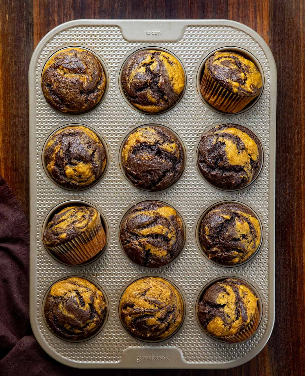Muffin pan filled with Pumpkin Chocolate Marble Muffins with a couple of muffins on their sides.