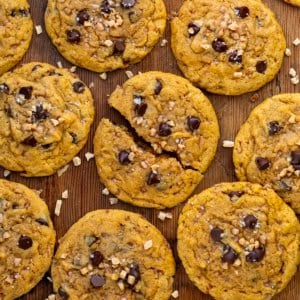 Pumpkin Toffee Chocolate Chip Cookies on a wooden table from overhead with the middle cookie broken in half.