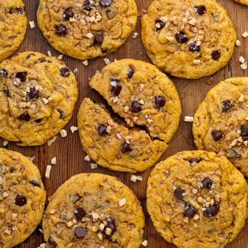 Pumpkin Toffee Chocolate Chip Cookies on a wooden table from overhead with the middle cookie broken in half.