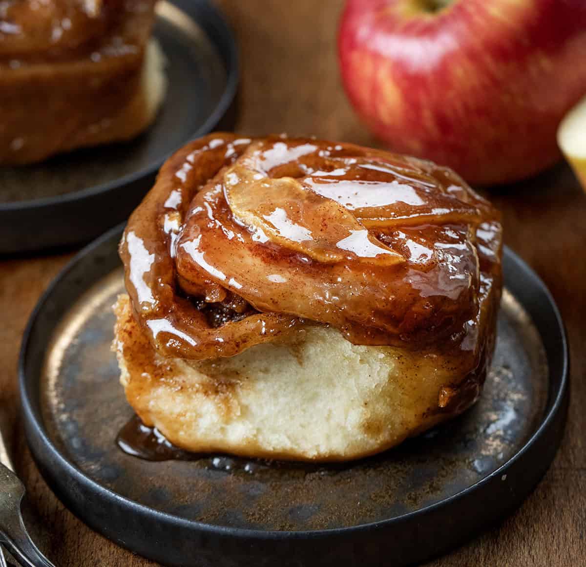 Apple Caramel Rolls on black plates on a wooden table with apples very close up.