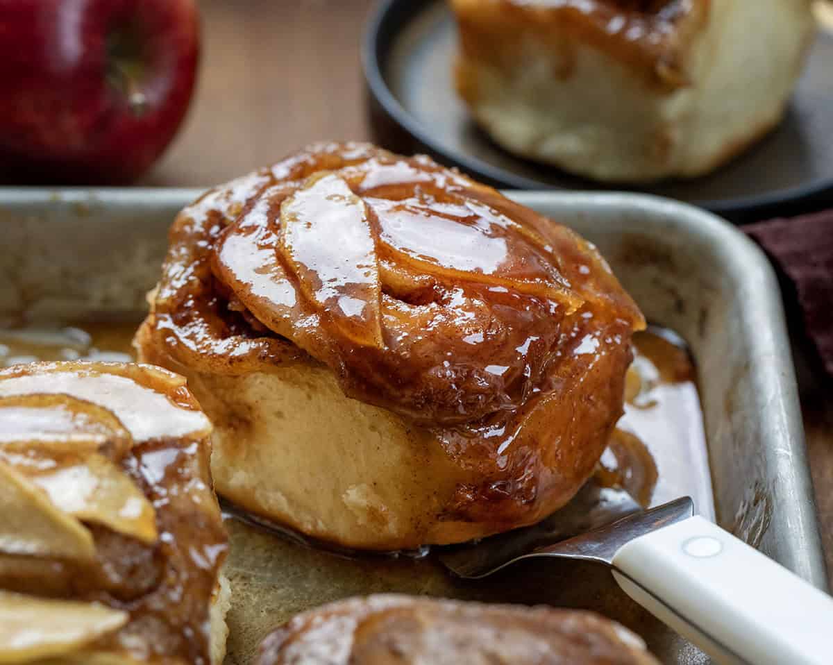 Close up of one Apple Caramel Roll sitting by others on the sheet pan.