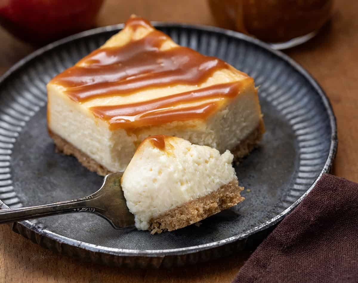 Fork taking a bite from Apple Cider Cheesecake Bar on a plate on a wooden table.